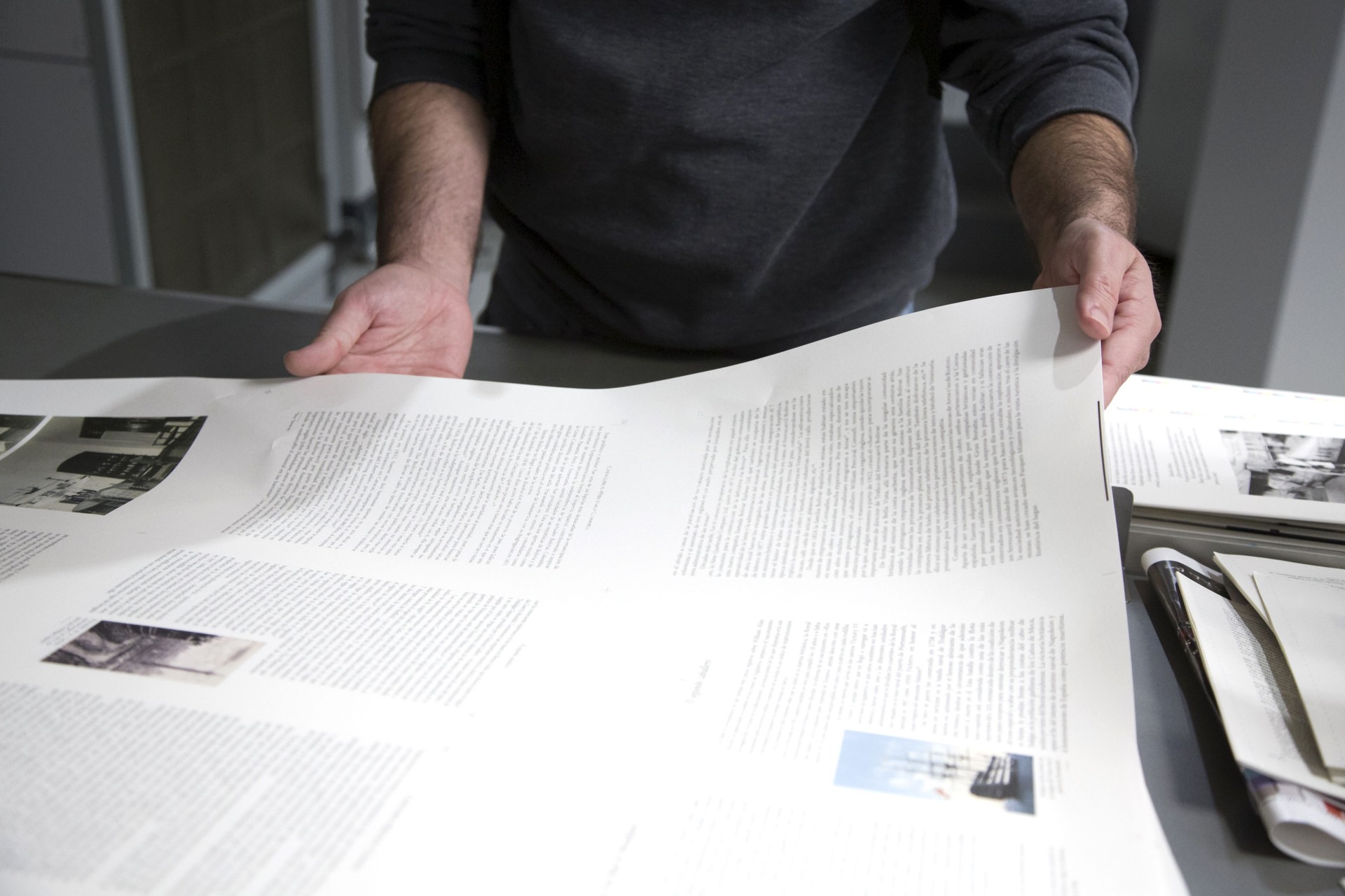 The man is holding a sheet of paper with the printed text in the printing house.
