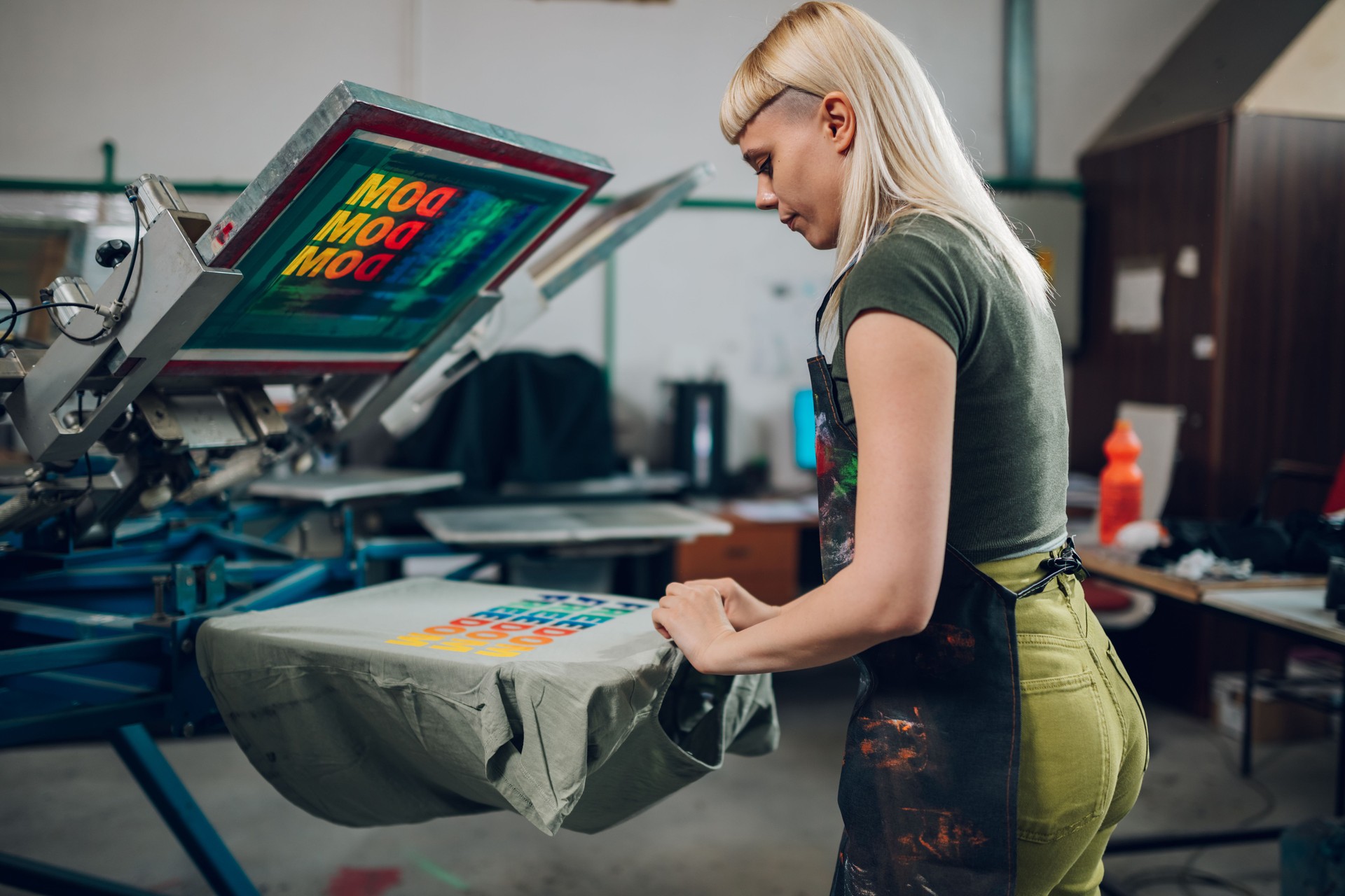 Print shop worker taking screen printed t-shirt of machine at facility